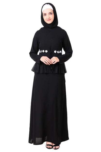 A woman wearing a traditional black abaya with frilled georgette waist and a-line cut. She is also wearing a matching square hijab.