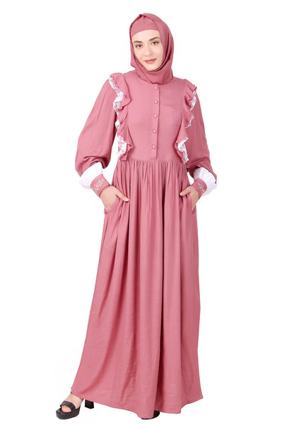 A dusty pink rayon abaya with embroidered fabric buttons on the placket, contrast frills embellishment on the bodice and sleeves, and straight sleeves with embroidered cuffs. The abaya includes utility seam pockets on both sides and is paired with a matching square hijab.