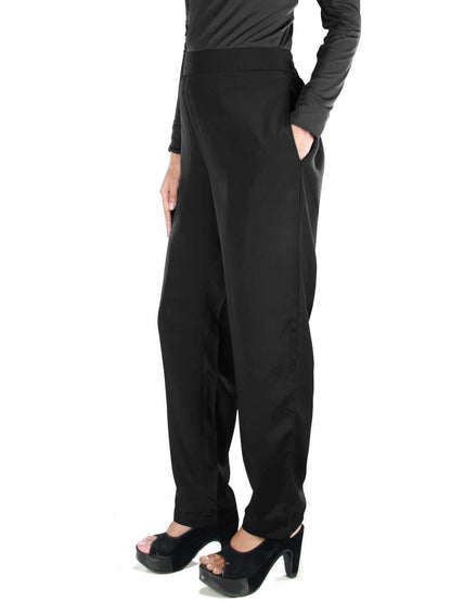 A person standing wearing black pants with a top waistband and elastic waist back, featuring narrow bottoms and utility pockets on the sides.