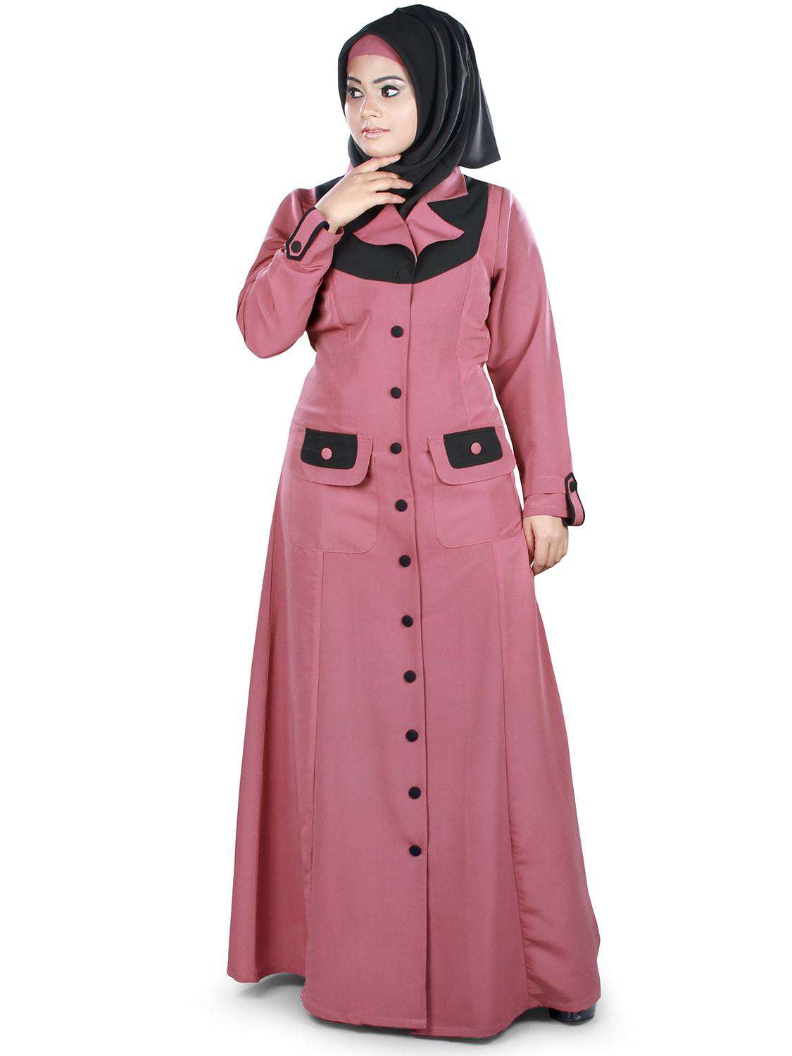 A woman wearing a pink jilbab with black collar and buttons, featuring straight sleeves and utility pockets on the sides.