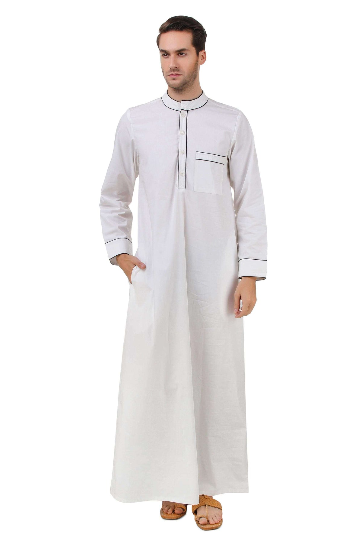 A man wearing a white cotton galabiyya with a band collar neckline, black piping finishing on the collar and chest pocket, and utility pockets on the sides.