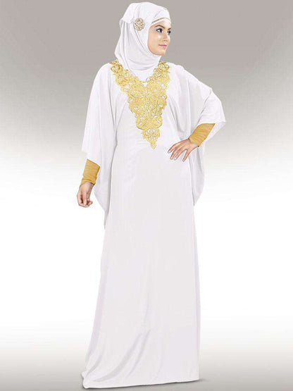 A woman wearing a white kaftan with gold embroidery at the neckline and a square hijab.