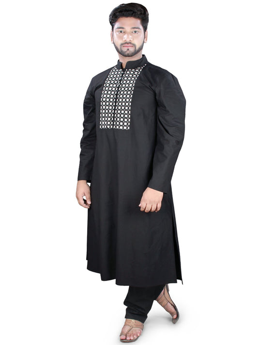 A person standing and posing in a black kurta pajama with embroidered neckline and side slits on the pants.