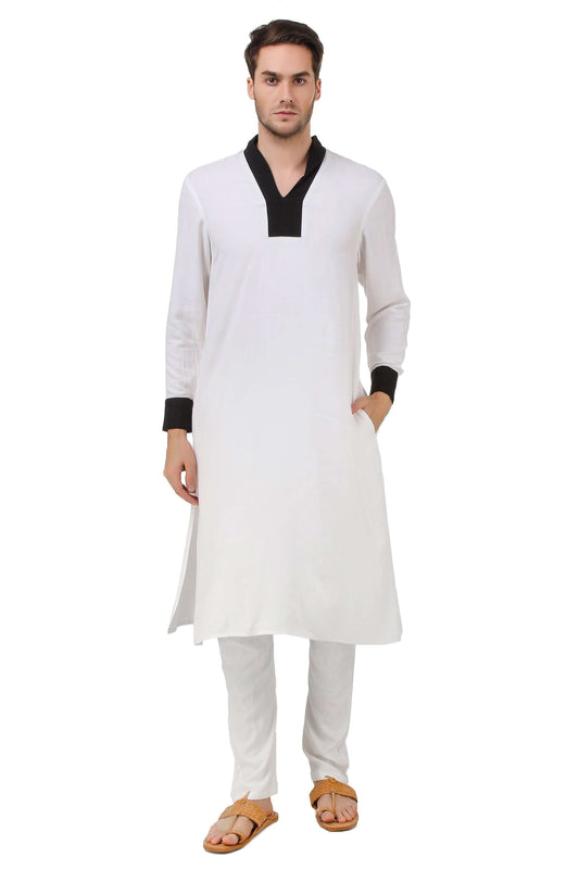 A man wearing a white kurta pajama set with contrast fabric shawl collar and 'V' neck opening, straight sleeves with contrast fabric cuffs, and drawstring waist pants.